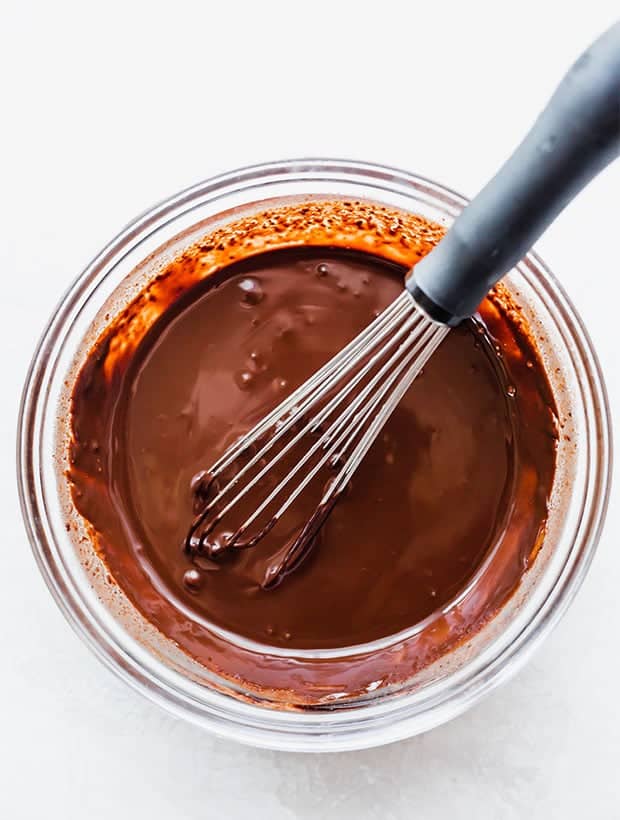 A glass bowl of melted chocolate with a wire whisk in the bowl. 