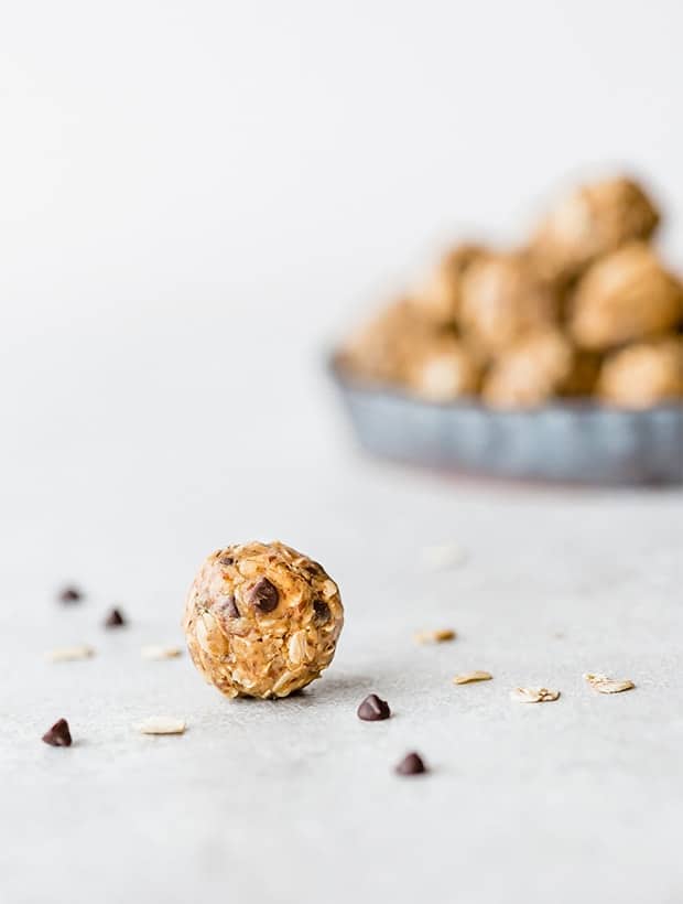 A no-bake energy bite in the foreground of the photo, with a stack of energy bites in the background. 