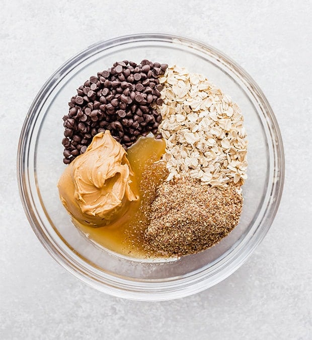 A glass bowl with oats, chocolate chips, peanut butter, flax seed, honey, and vanilla; prepping to make no-bake energy bites.