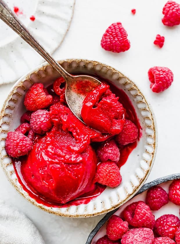 A bowl of raspberry sorbet and a spoon scooping up a portion of the sorbet.