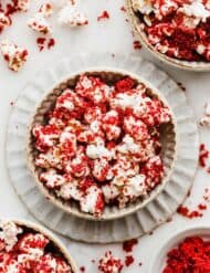 A bowl in the center of the photo full of red velvet popcorn with red velvet cake crumbs surrounding the bowl.