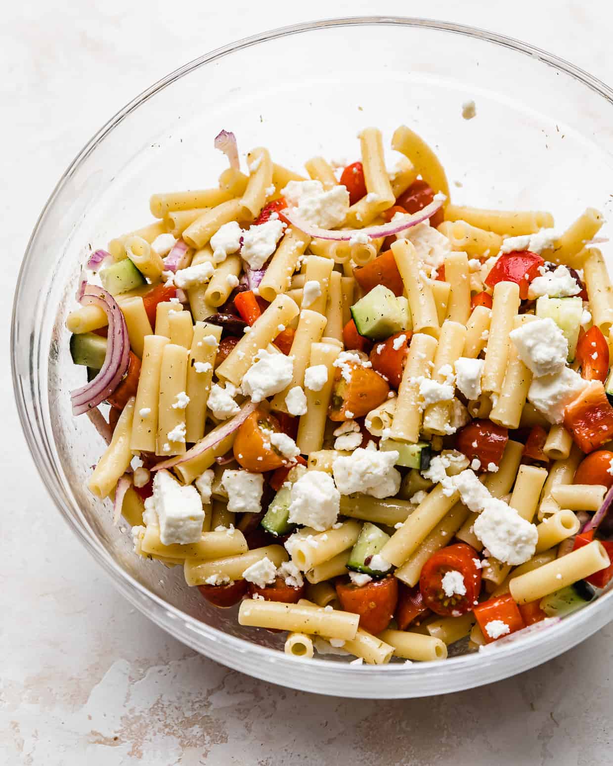 Greek pasta salad with ziti noodles in a glass bowl topped with feta cheese.