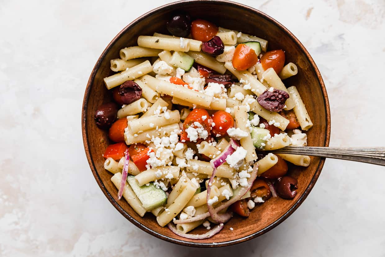 A brown bowl with Summer Fresh Greek Pasta Salad topped with feta cheese.