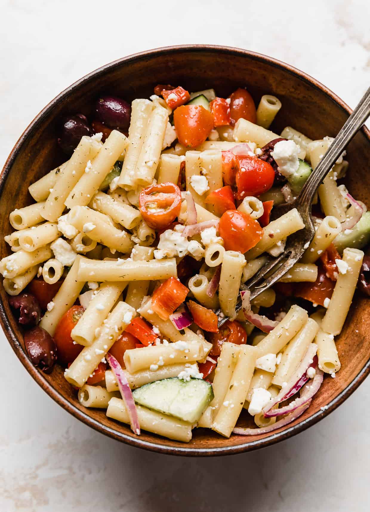A brown bowl with penne Summer Fresh Greek Pasta Salad in it.
