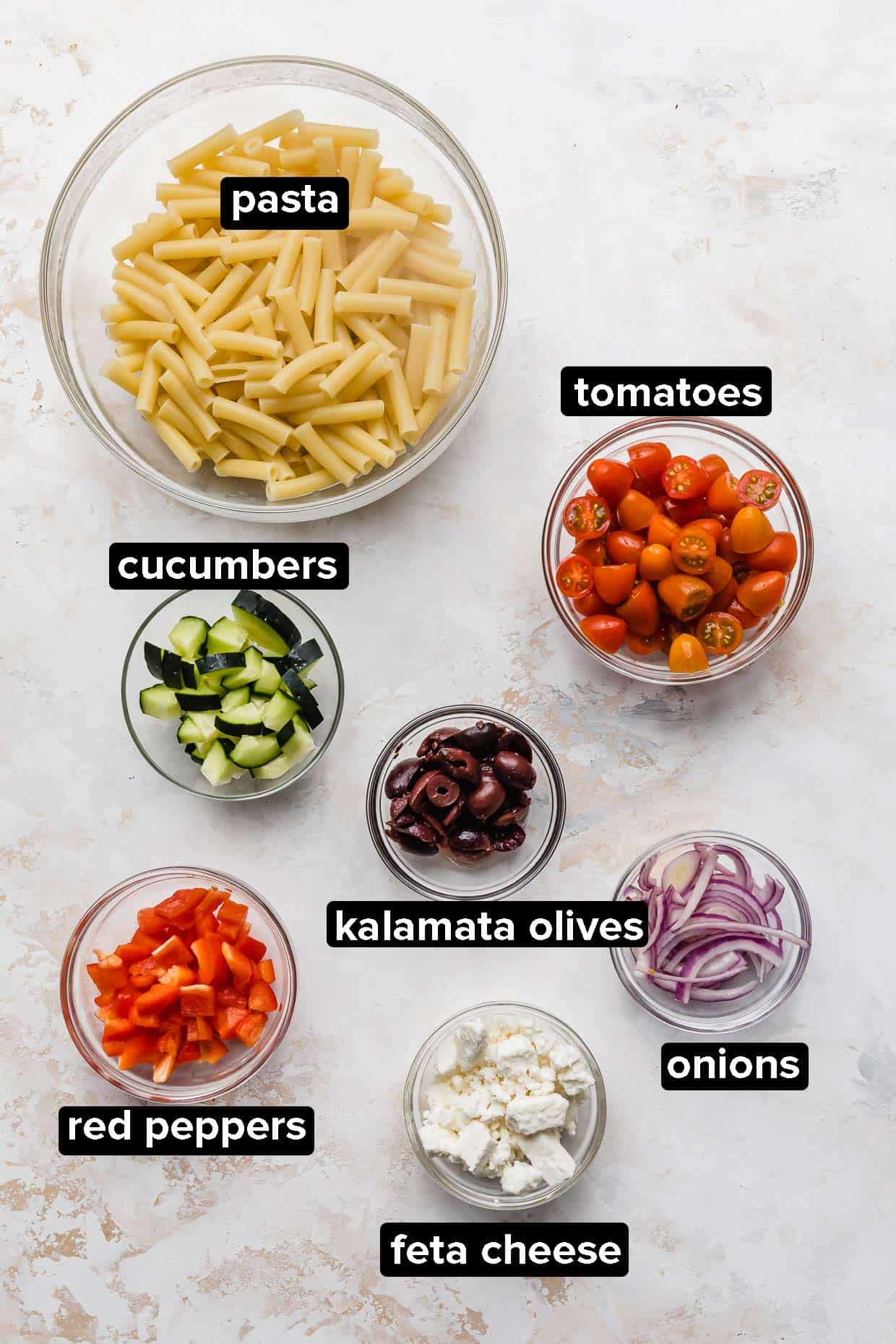 Ingredients used to make a summer greek pasta salad on a white background.