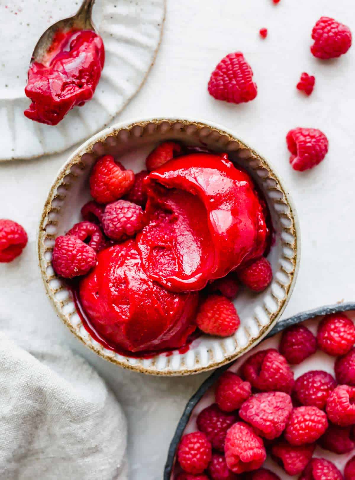 A bowl filled with bright red fresh Raspberry Sorbet on a white background.