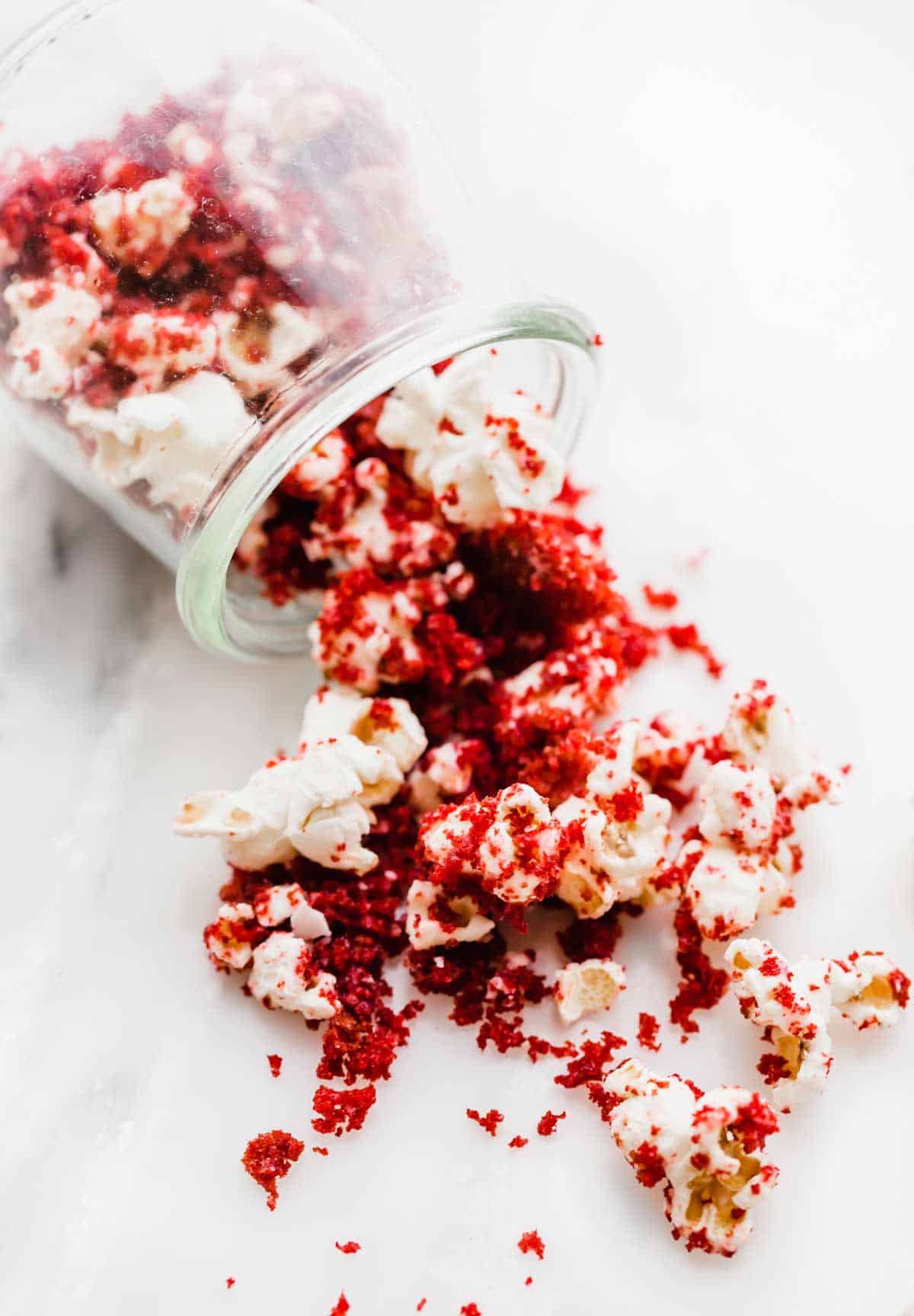Red Velvet Popcorn spilling onto a white table from a glass cup.