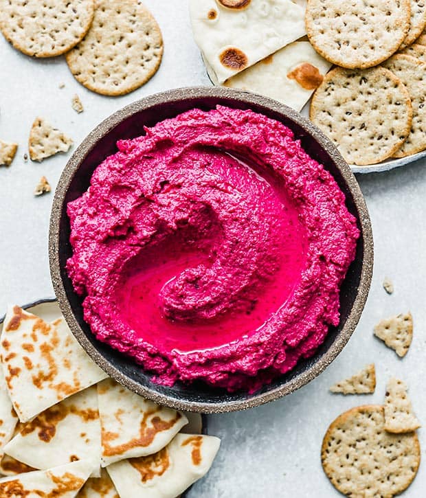 Beet hummus surrounded by crackers.