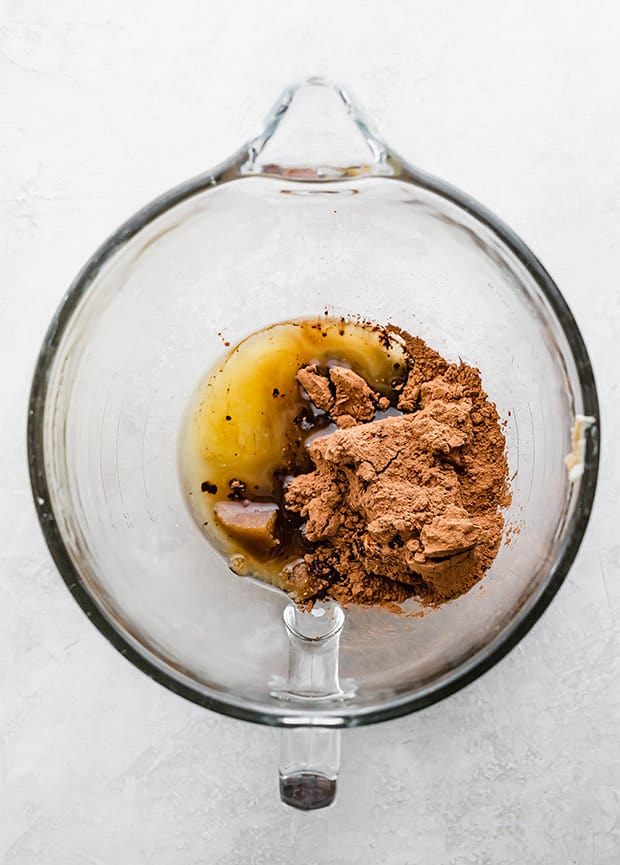 A glass bowl with cocoa, melted butter, sugar, and oil in preparation to making a brownie cookie recipe.