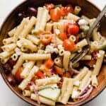 Close up photo of a fresh greek pasta salad with penne noodles in a brown bowl.
