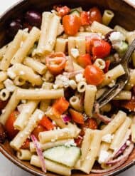 Close up photo of a fresh greek pasta salad with penne noodles in a brown bowl.