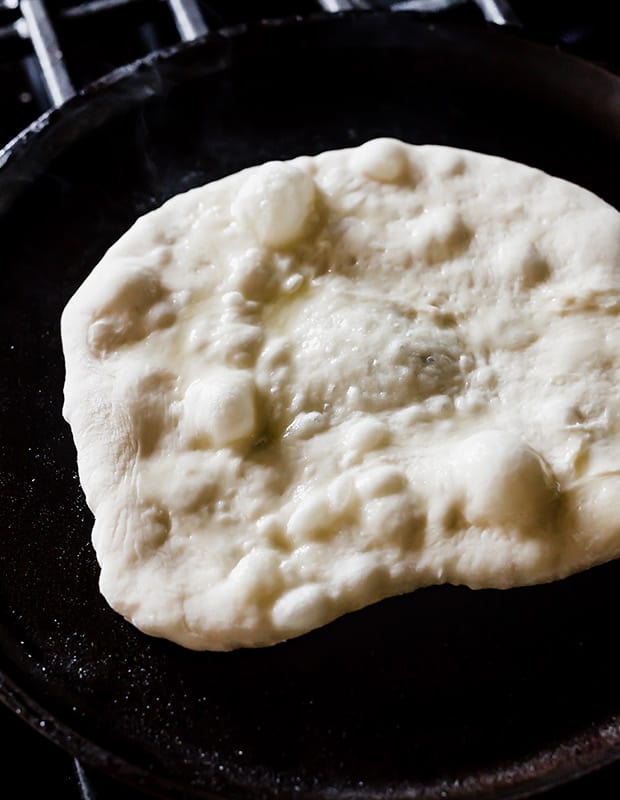 Naan bread on a cast iron skillet with bubbles forming as it cooks.