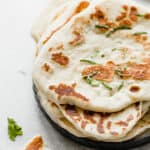 Naan bread on a plate with a small garnish of chopped cilantro.