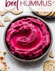 Beet Hummus in a black bowl surrounded by crackers and naan bread.