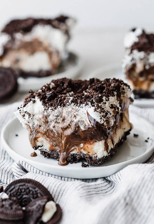 Delicious Oreo Ice Cream Cake on a white plate with hot fudge melting down the sides.