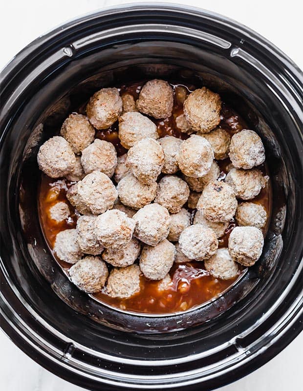 A slow cooker full of barbecue sauce, crushed pineapple, and frozen meatballs.