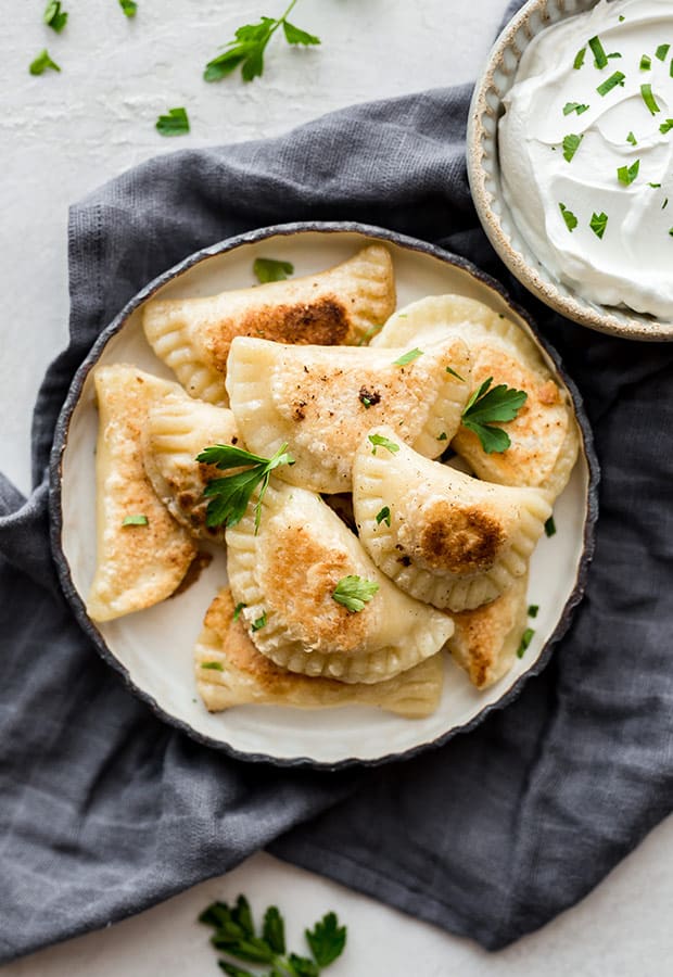 Overhead photo of a plate full of homemade pierogies with a bowl of sour cream to the side of the plate.