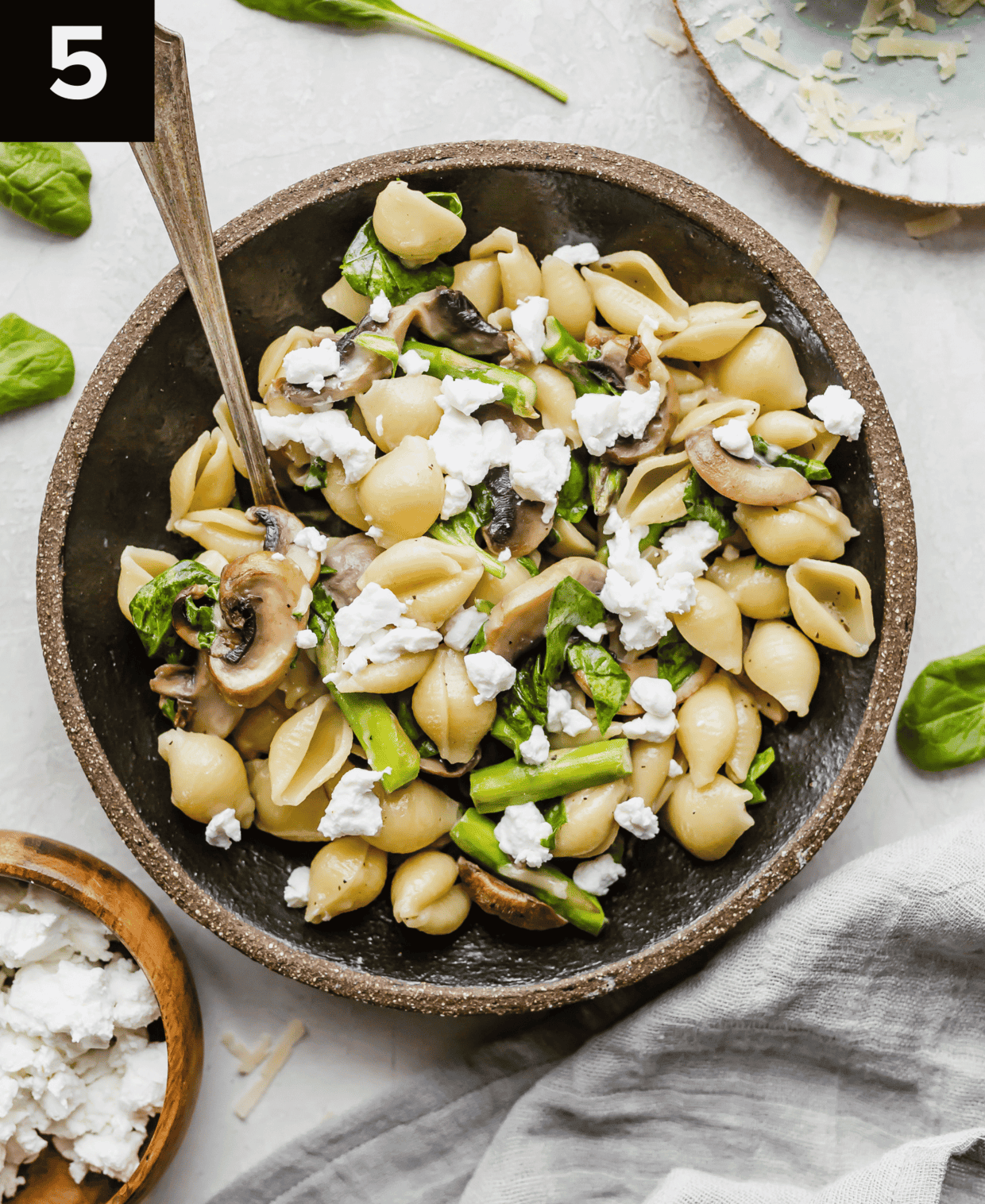 Asparagus Spinach Pasta topped with goat cheese, in a black bowl on a white background.