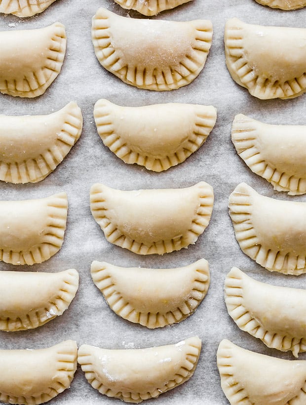 Overhead photo of filled and folded homemade pierogies lined up on a baking sheet.