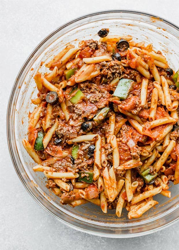 Penne pasta noodles mixed into marinara sauce and pizza toppings for pizza casserole recipe.