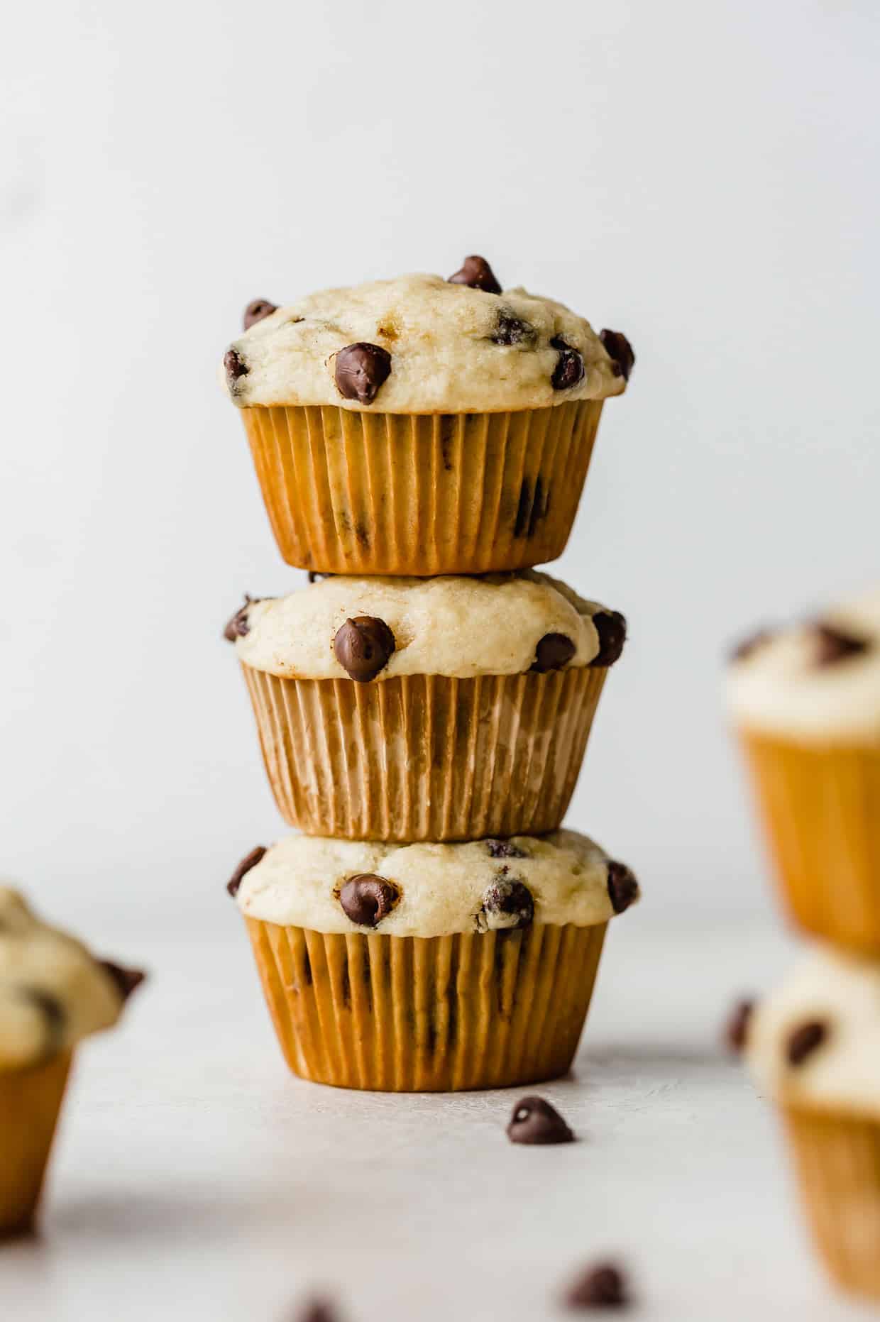 Three Buttermilk Banana Chocolate Chip Muffins stacked on top of each other against a white background.