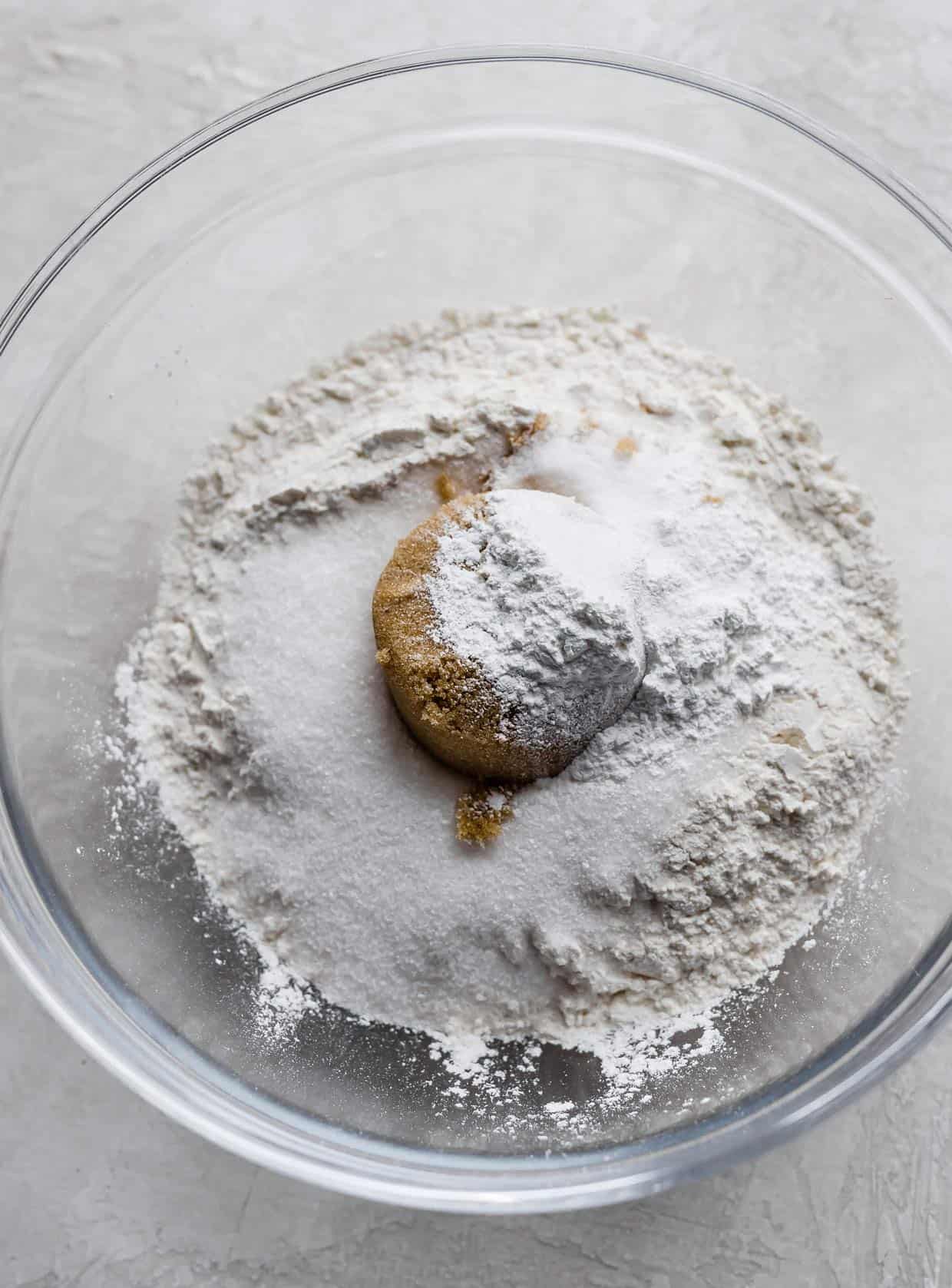 Flour, brown sugar, sugar and other white dry ingredients in a glass bowl.