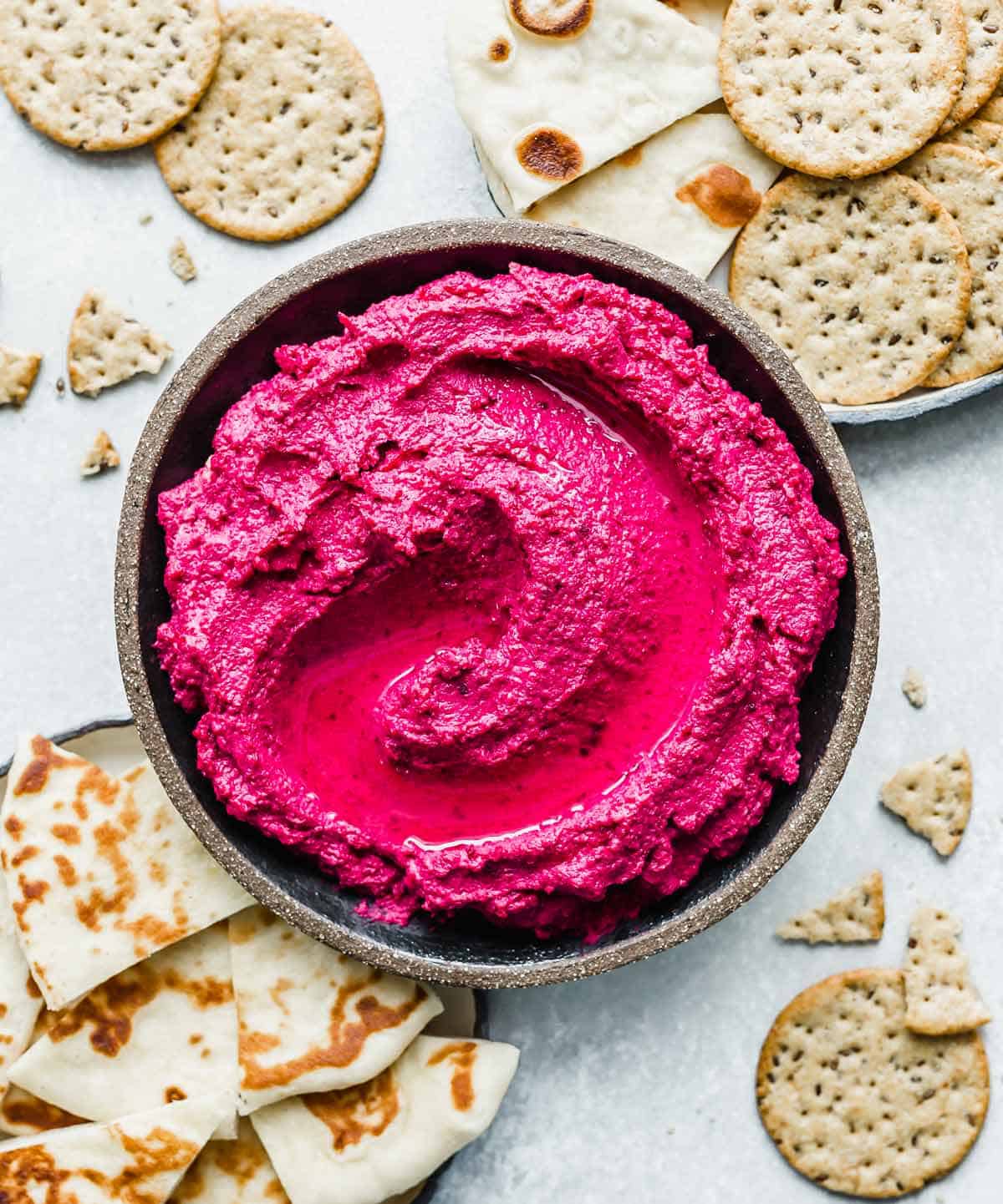 Beet Hummus in a round bowl surrounded by naan and crackers.
