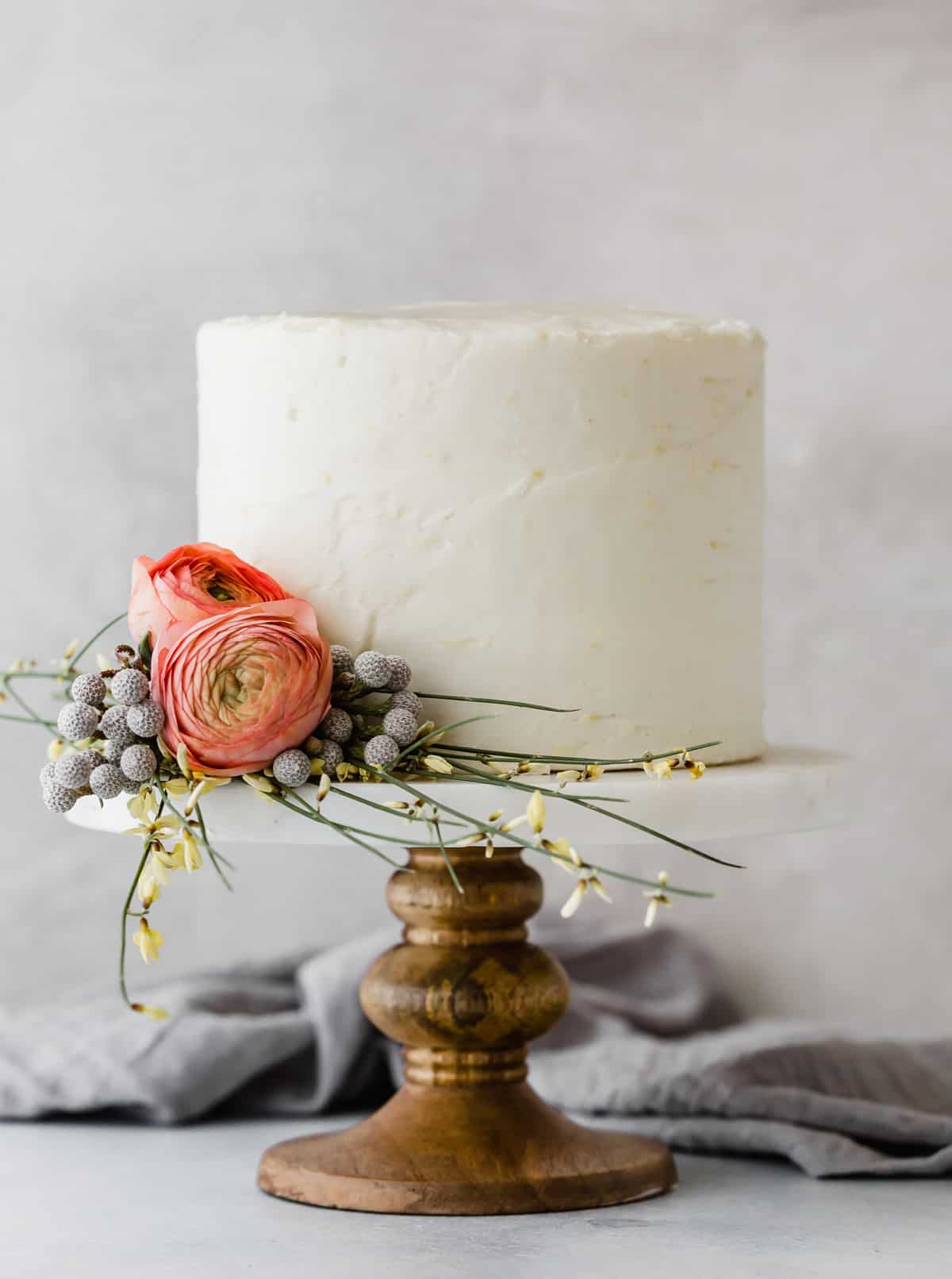 A Lemon Poppy Seed Cake with Cake Mix layered cake on a wooden cake stand covered in a white buttercream frosting.