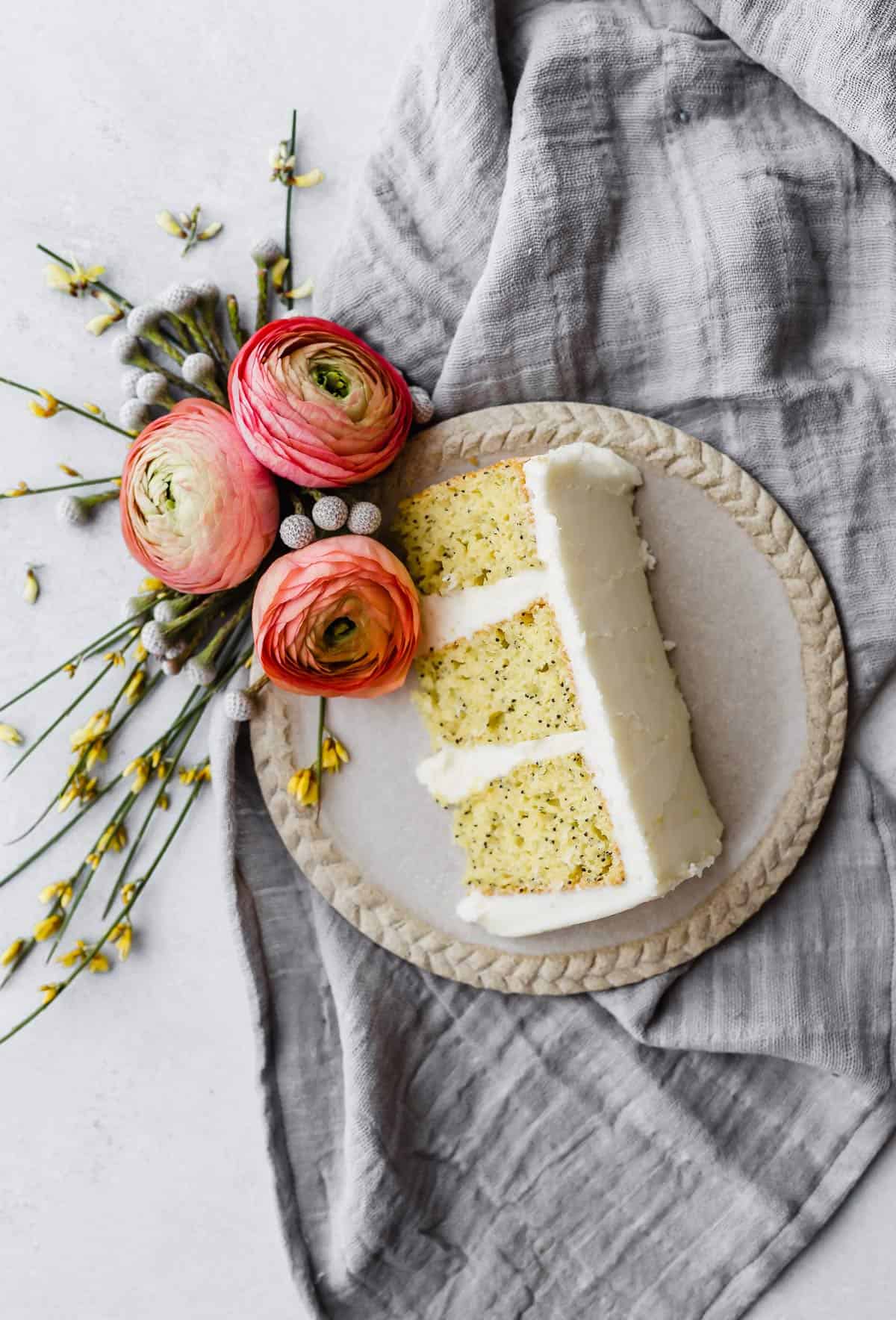 A slice of Lemon Poppy Seed Cake made with Cake Mix on a plate with three pink flowers near the cake.