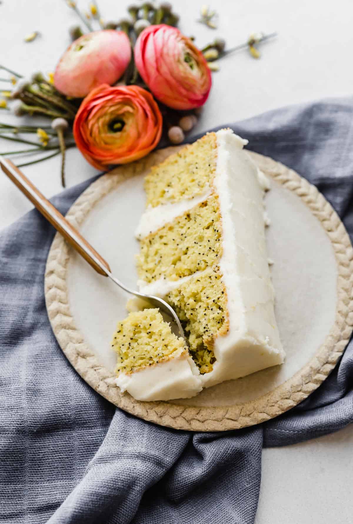 A fork cutting into a slice of lemon poppy seed layer cake on a tan plate.