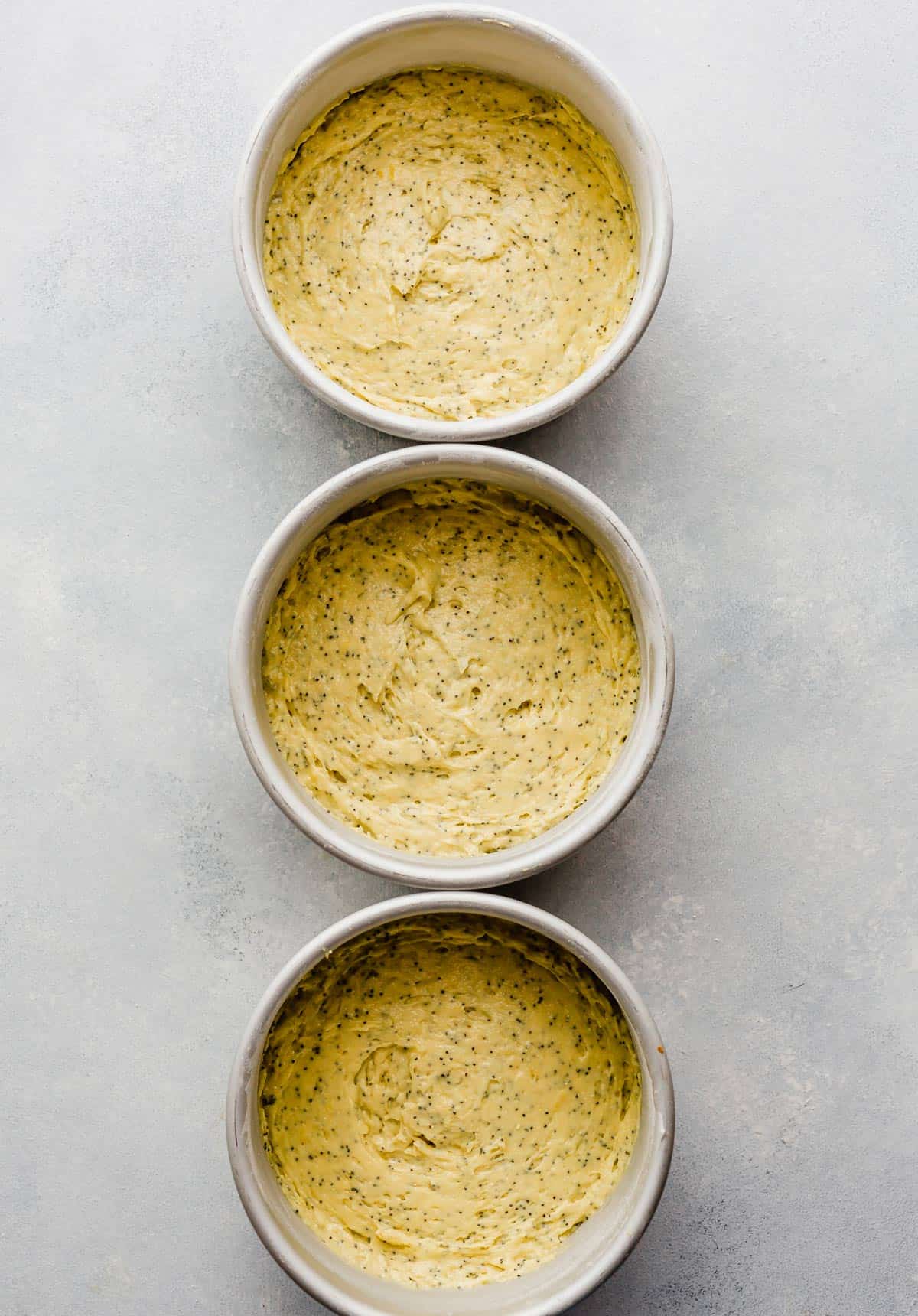 Three six inch round cake pans filled with lemon poppy seed cake batter.