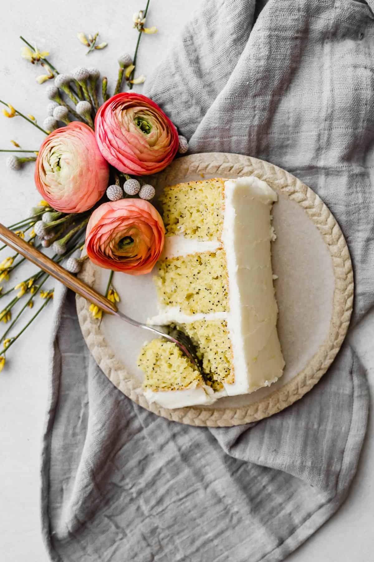 A slice of lemon poppy seed layered cake made from a cake mix on a plate that's resting on a gray napkin.