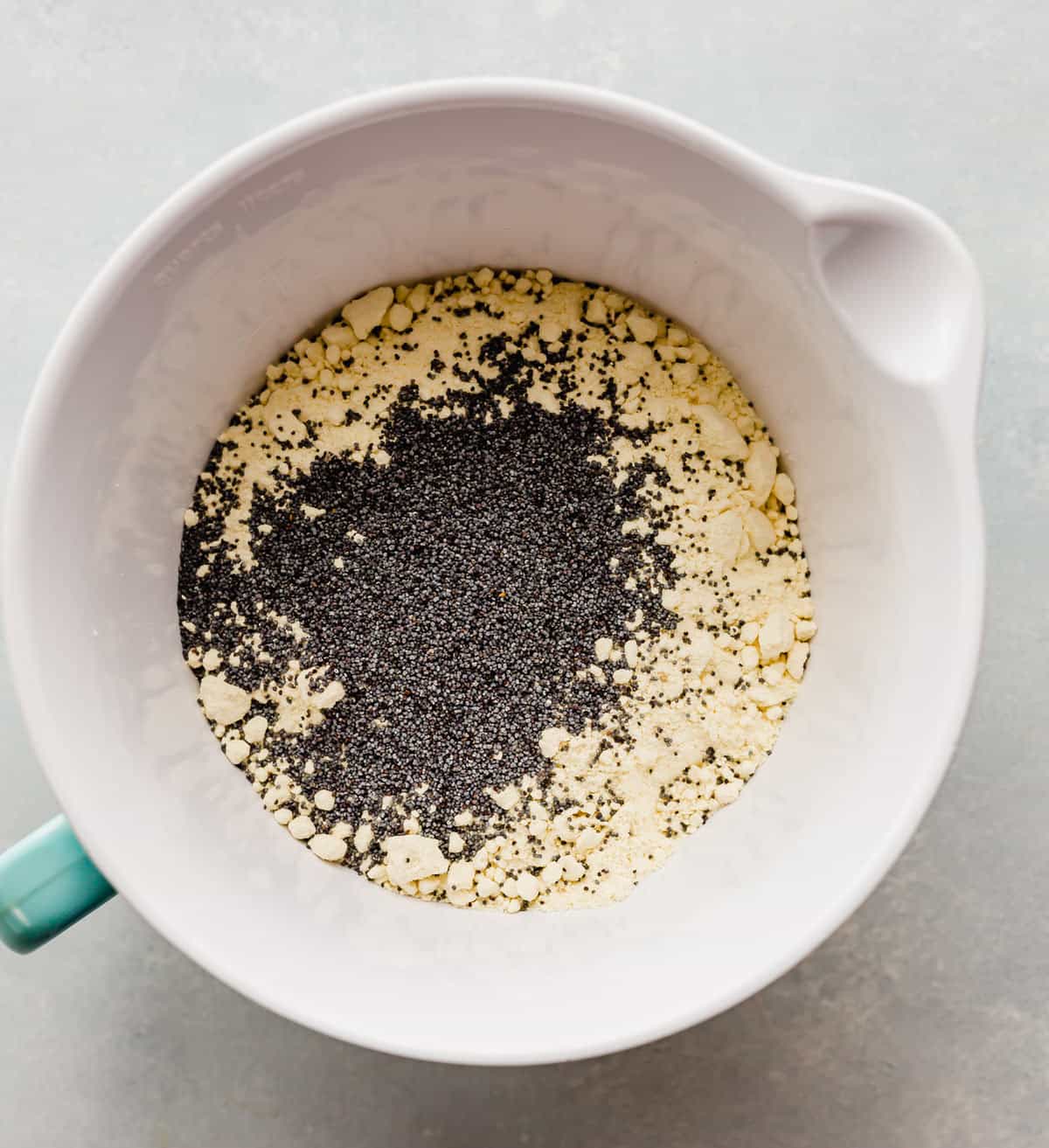 A white bowl with dry ingredients and poppyseeds in it for making Lemon Poppy Seed Cake with Cake Mix.