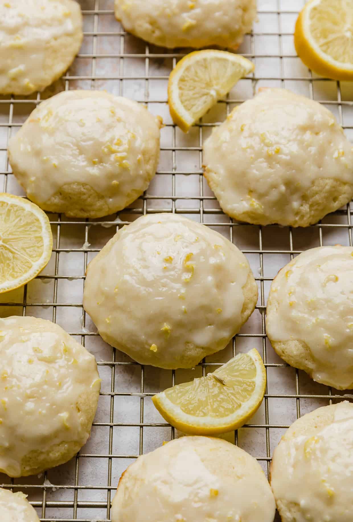 Glazed Lemon Ricotta Cookies on a wire rack surrounded by sliced lemons. 
