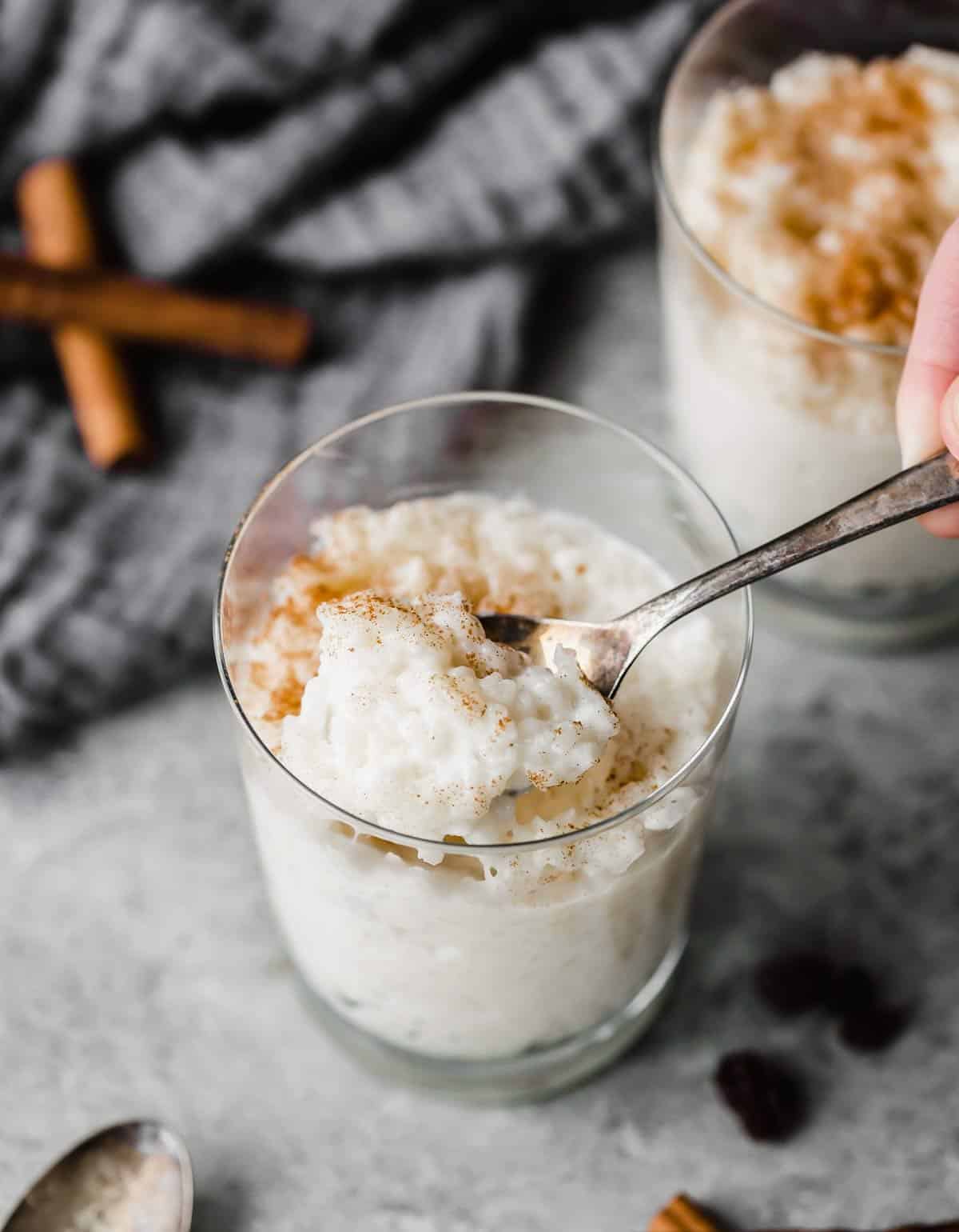 A glass cup filled with white Mexican Rice Pudding (Arroz con Leche) topped with a sprinkle of ground cinnamon.