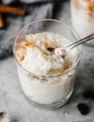 A spoon scooping out Mexican Rice Pudding (Arroz con Leche) from a glass cup on a gray background.