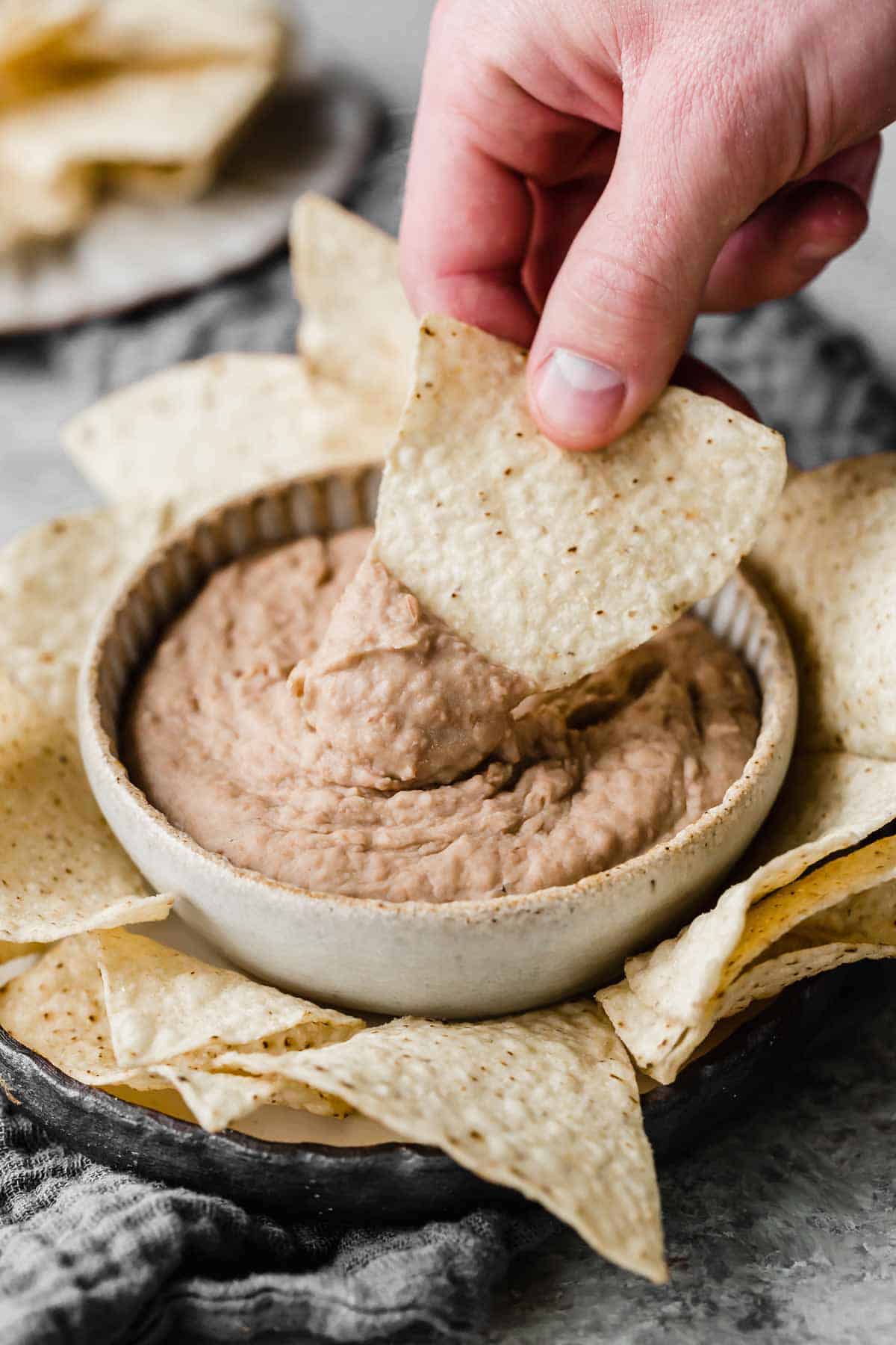 A tortilla chip being dipped into a bowl filled with homemade refried beans.
