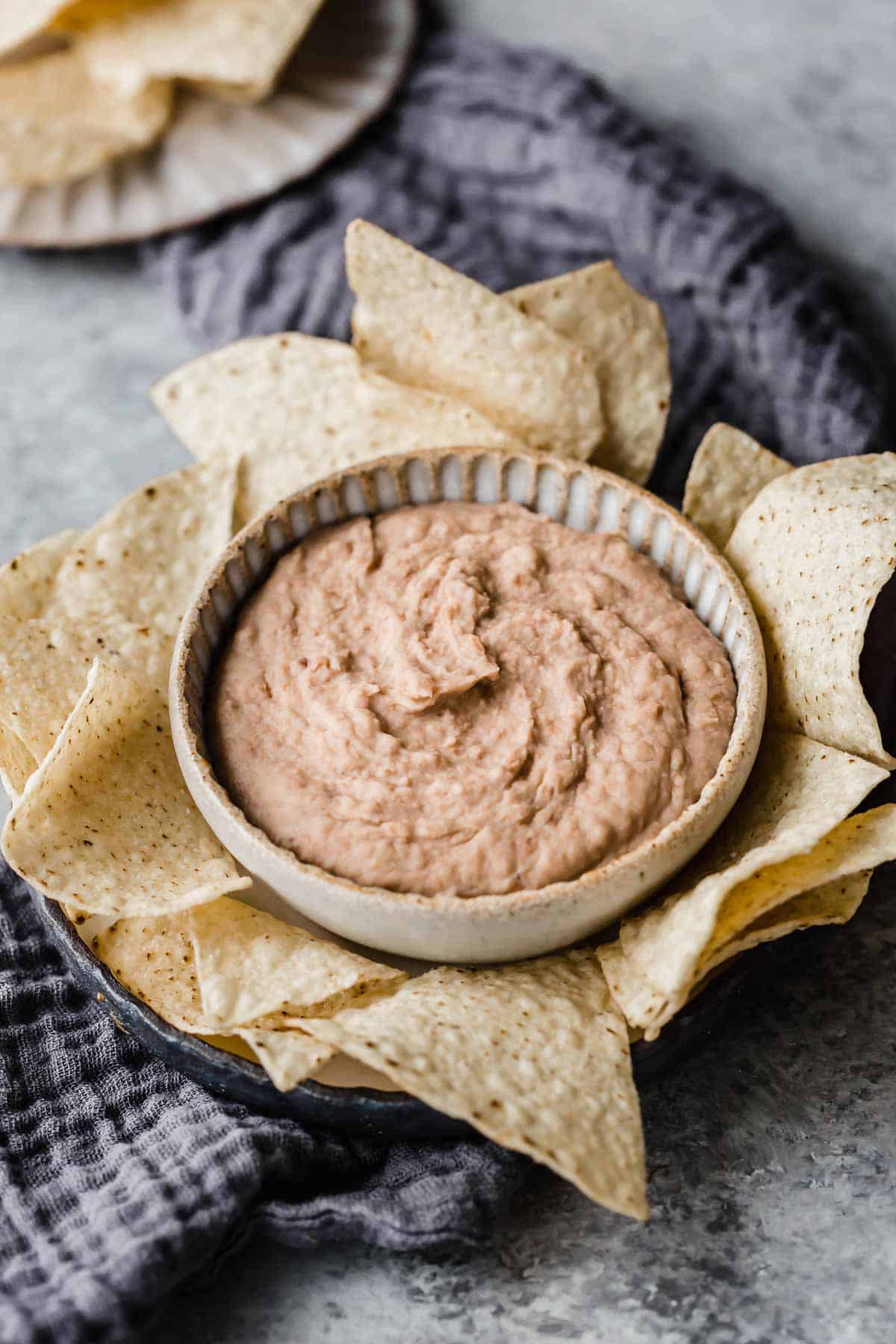 Crock pot refried beans in a handmade ceramic bowl with tortilla chips surrounding the bowl.