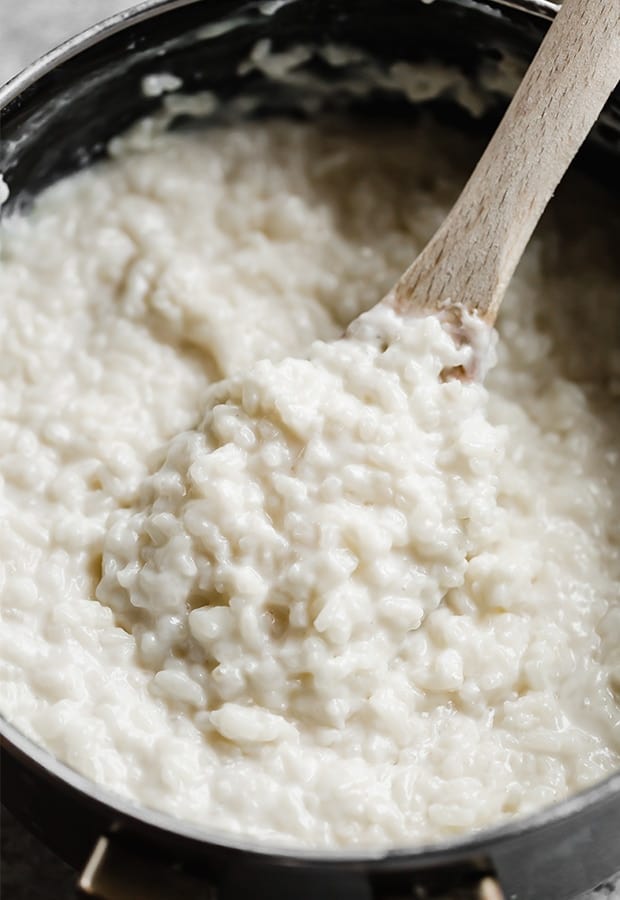 A close up photo of a wooden spoon scooping out a portion of the completed Mexican rice pudding also known as Arroz con Leche.