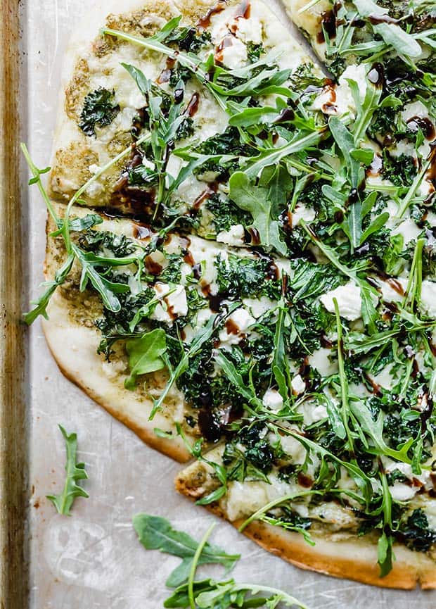 A close up of a kale pizza topped with arugula and goat cheese with a drizzle of balsamic glaze.