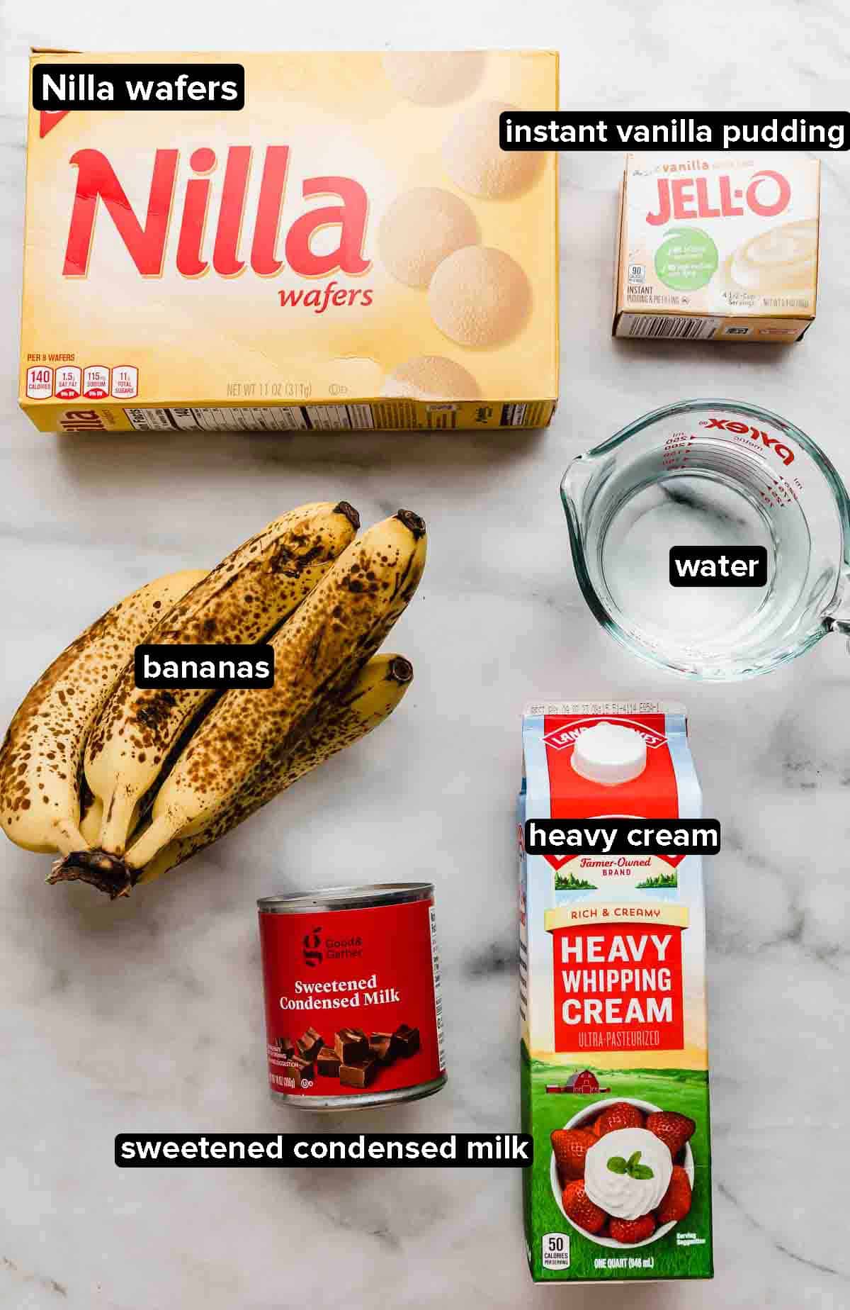 Magnolia Bakery Banana Pudding ingredients on a marble background: Nilla wafer crackers, vanilla jello, heavy cream, bananas, water, sweetened condensed milk.
