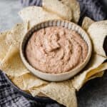 Slow Cooker Refried Beans in a bowl surrounded by tortilla chips.