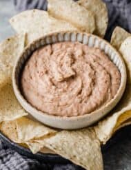 Slow Cooker Refried Beans in a bowl surrounded by tortilla chips.