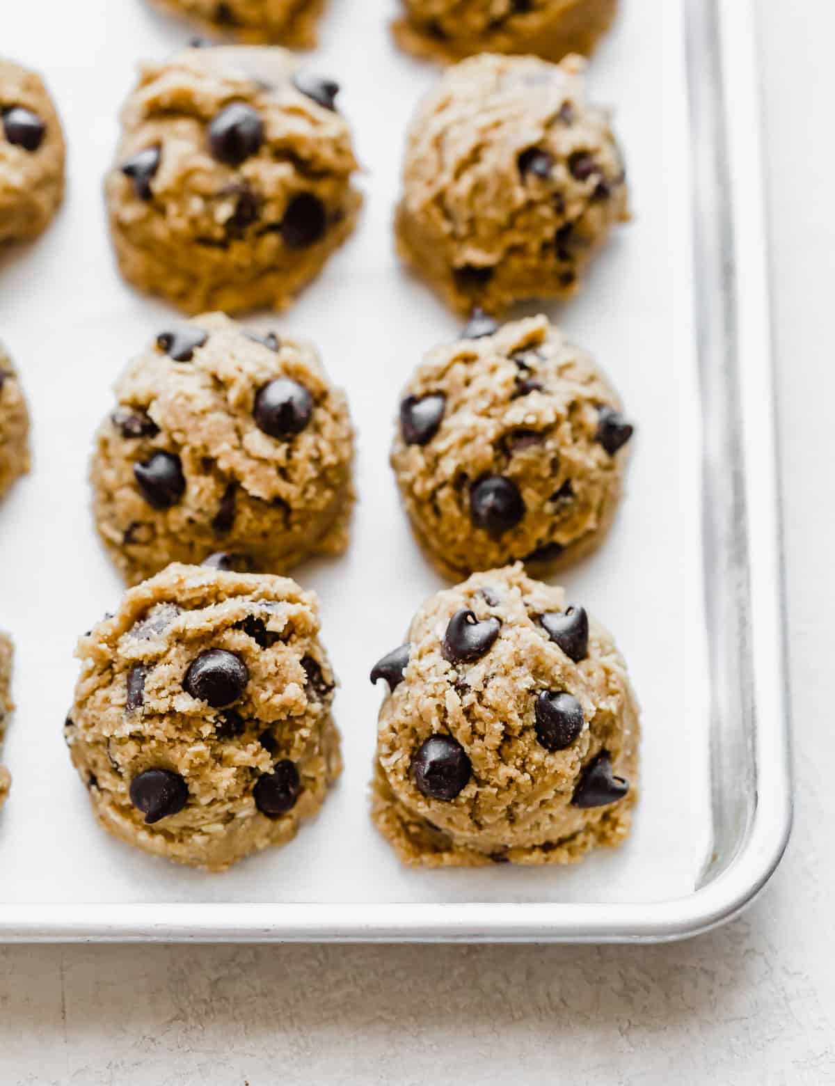 Brown Butter Chocolate Chip Cookie dough balls topped with chocolate chips, in a row on a baking dish.