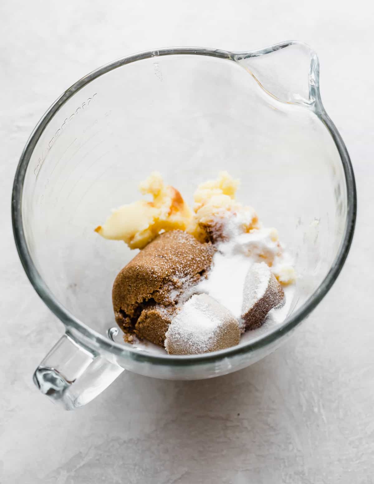 Sugar, brown sugar, and brown butter in a glass stand mixer bowl.