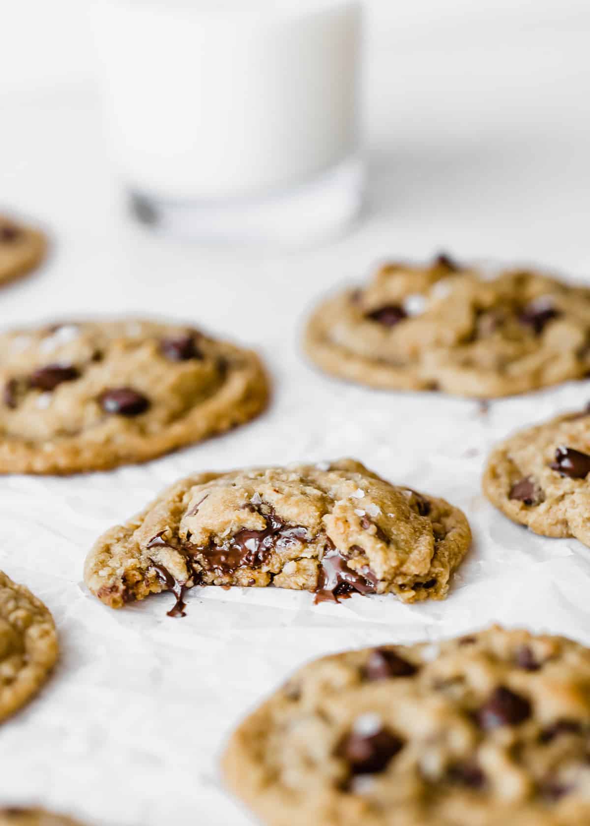 A Brown Butter Chocolate Chip Cookie with a bite taken out of it, on a white parchment paper.