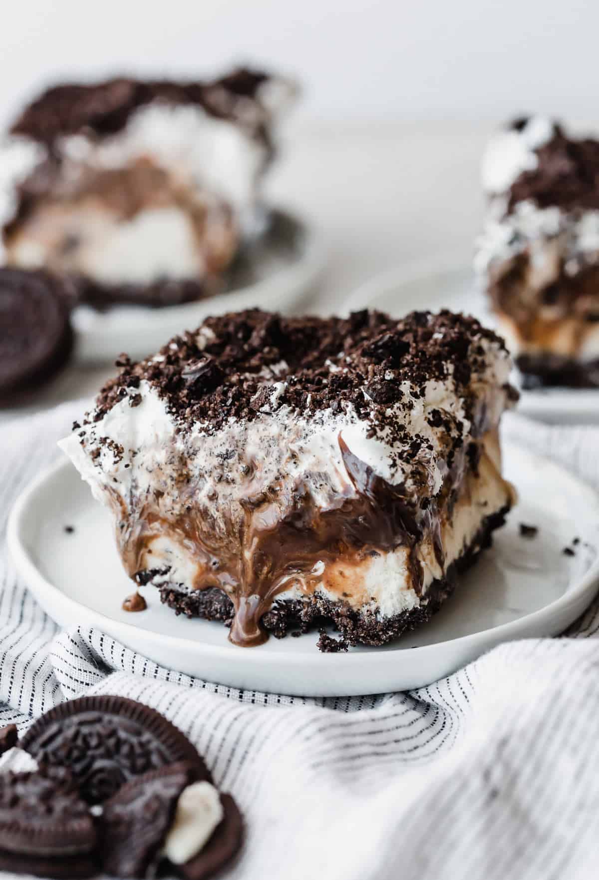 A square slice of Oreo Ice Cream Cake topped with hot fudge, whipped topping and crushed Oreos.