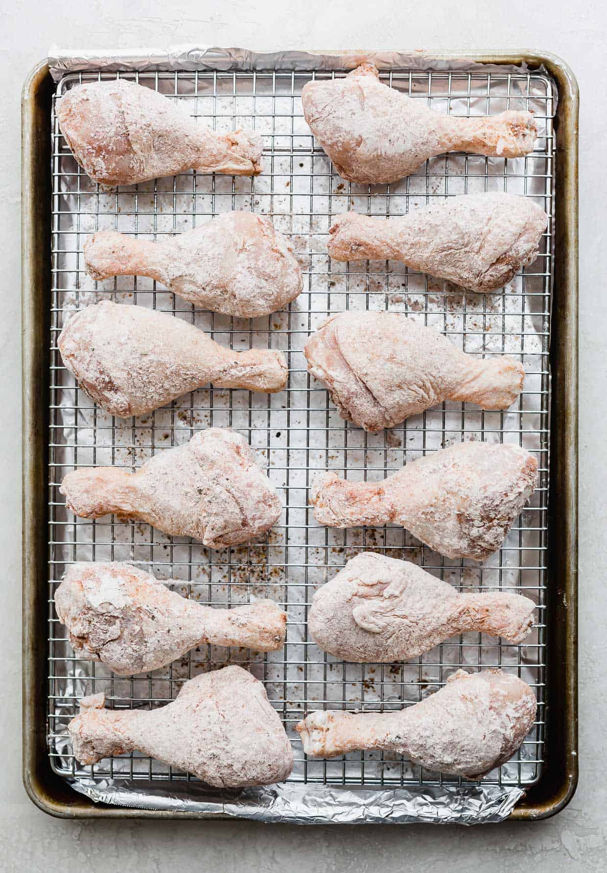 Flour coated chicken drumsticks on a wire rack nested baking sheet. 