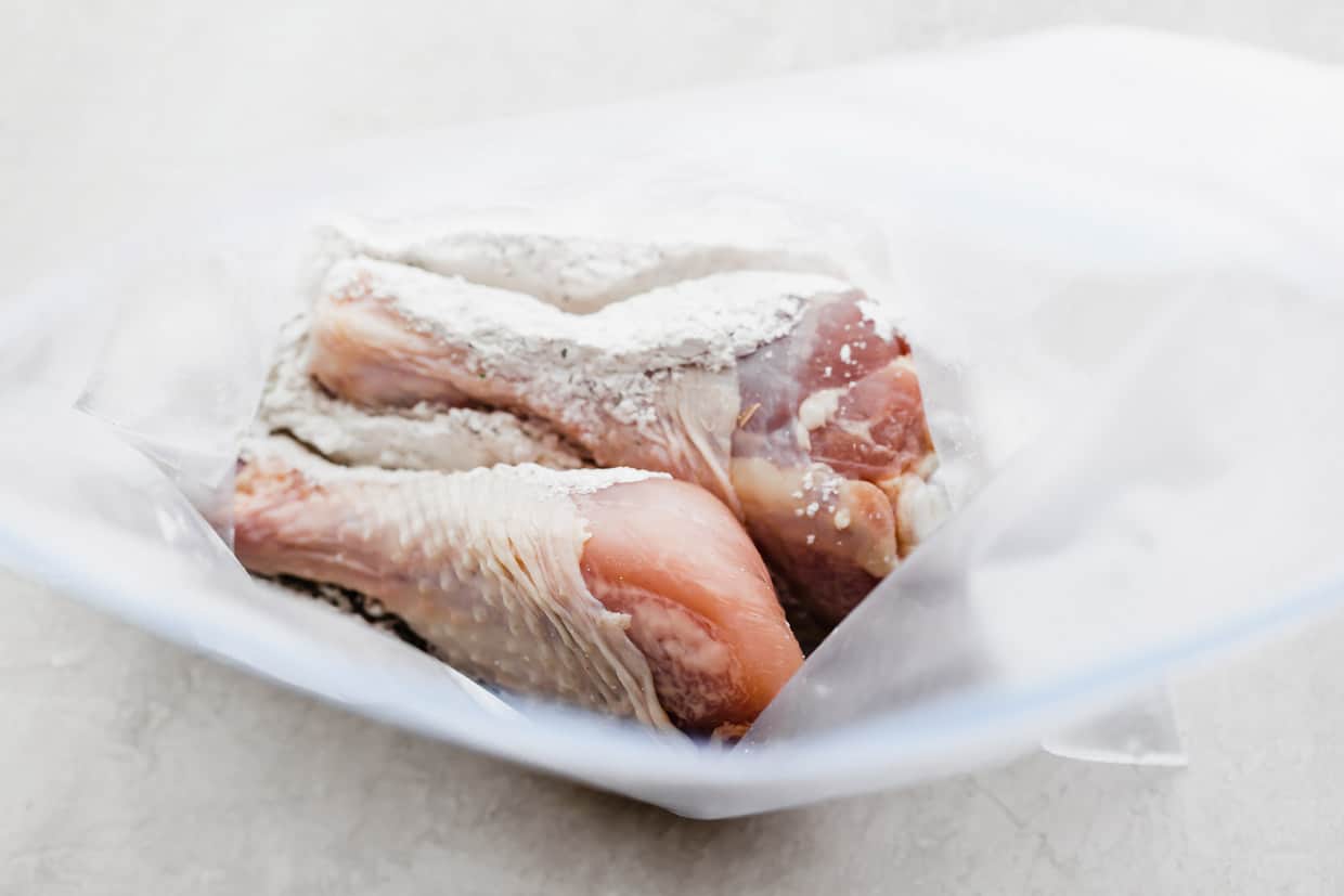 Two raw chicken legs in a ziplock bag on a white background.