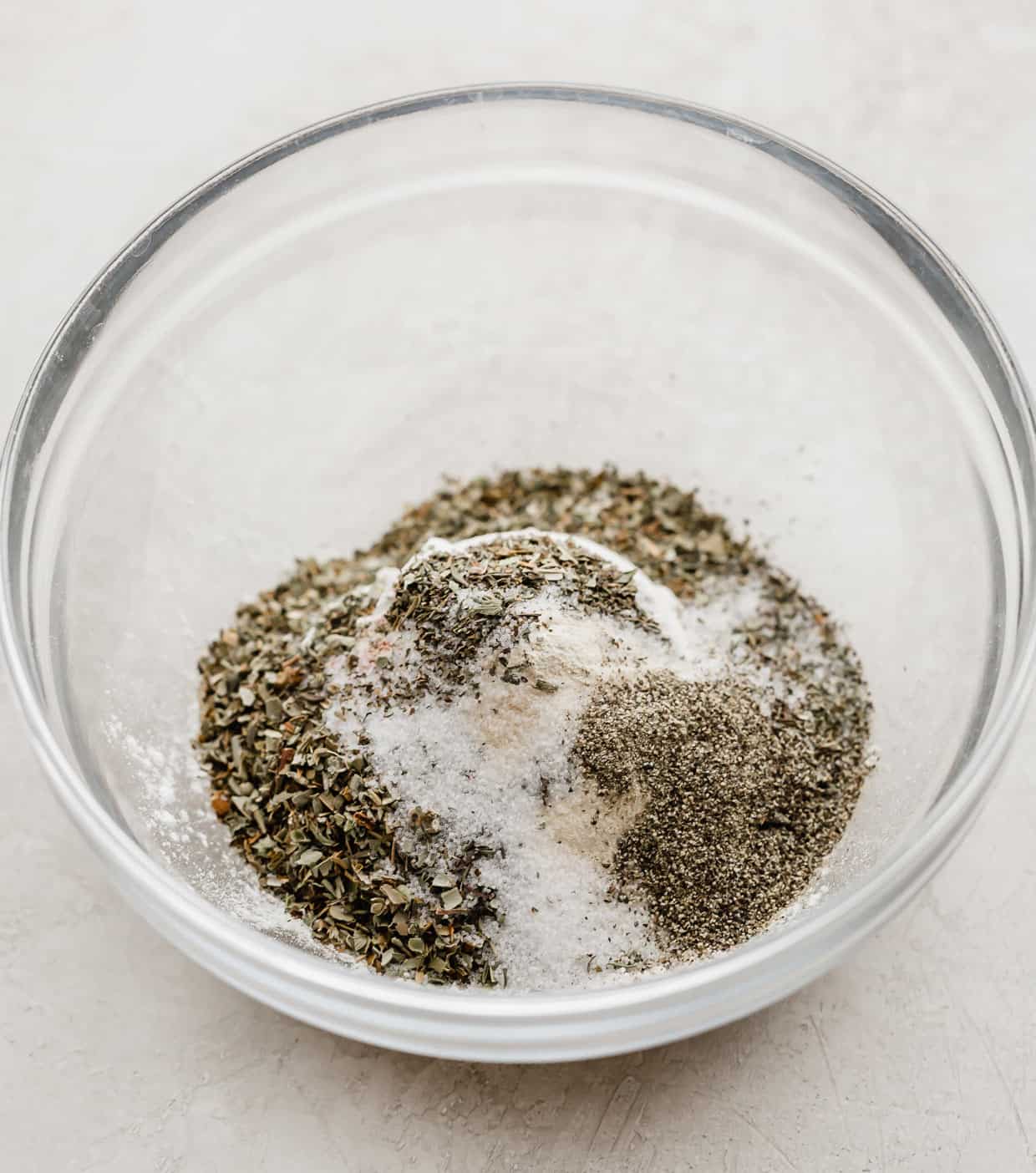 A glass bowl with flour, cornstarch, and a variety of dried herbs in it.